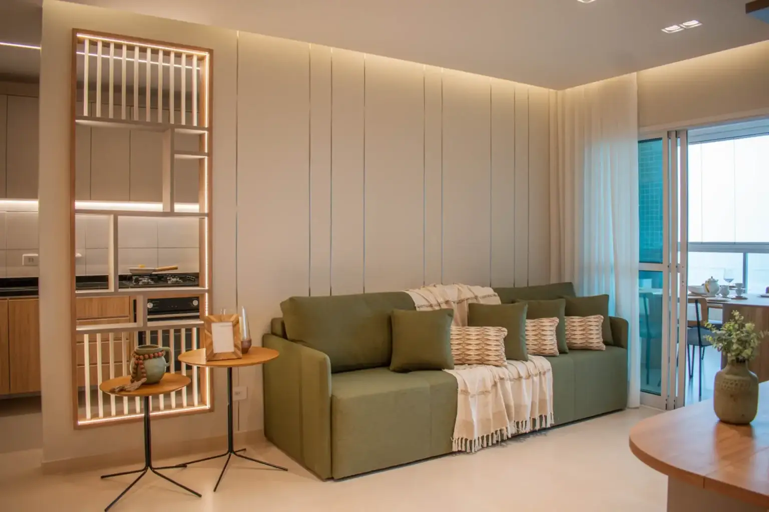 Sala de apartamento reformado com sofá verde, painel ripado e integração com a cozinha